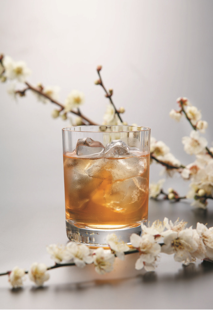 un verre rempli avec des glaçons et du umeshu, et des fleurs de prune en décoration